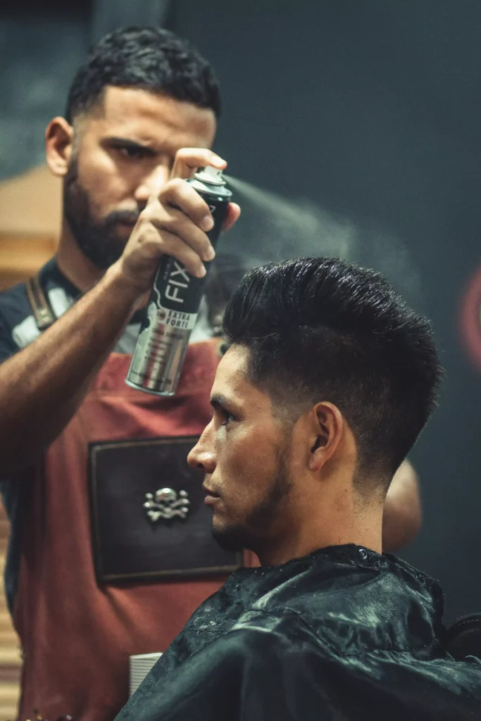 "Barber applying hair spray to a man's styled haircut in a professional grooming session at a men’s salon."